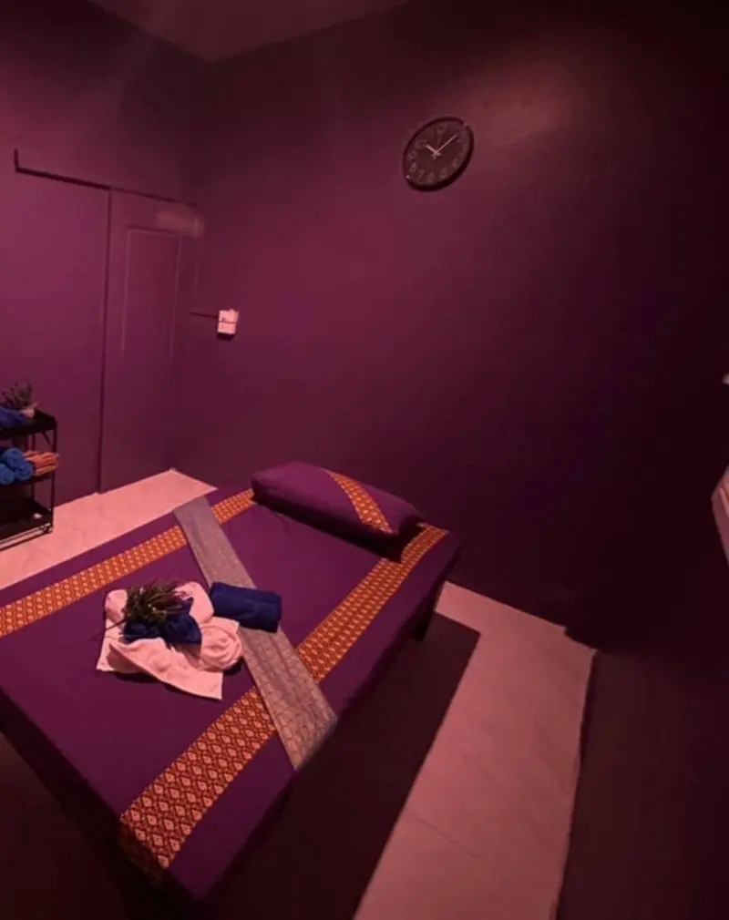 Treatment room with a purple massage bed, Thai-pattern runner and folded towels